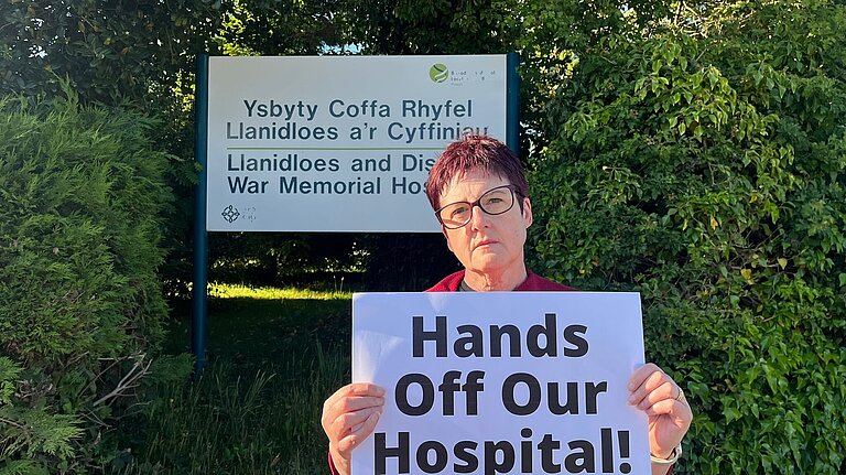 Fleur outside Llanidloes Hospital holding a sign that reads: "Hands off our hospital"